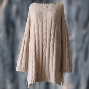 Puede incluir: Un suéter beige de punto trenzado con cuello redondo y mangas largas. El suéter tiene un ajuste relajado y una apariencia texturizada. La prenda está hecha de un material suave y cálido, perfecto para climas más frescos. Es una prenda versátil.