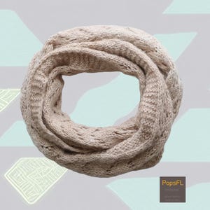 May include: A beige knitted infinity scarf with a delicate openwork pattern. The scarf is soft and cozy, perfect for keeping warm in the winter.