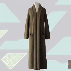 May include: Olive green longline cardigan with a shawl collar and two front pockets. The cardigan is displayed on a mannequin and worn over a white roll neck. The garment is floor-length and made of a soft, textured material.