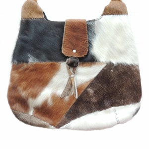 May include: A patchwork leather handbag with a brown flap and a silver button. The bag is made of different shades of brown, white, and black cowhide.