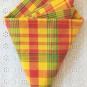 Peut inclure: Une serviette en tissu à carreaux jaunes, rouges et verts pliée en triangle.