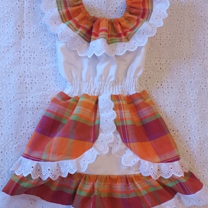 May include: A white dress with a red, orange and green plaid skirt and a white lace trim. The dress has a ruffled neckline and a white bodice.
