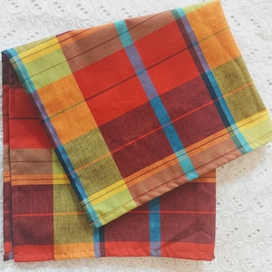 May include: Two red, orange, yellow, green, and blue plaid kitchen towels. The towels are folded on top of each other.
