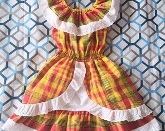 May include: A yellow, red, and green plaid dress with white lace trim. The dress has a ruffled skirt and a gathered bodice.