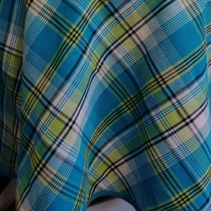 May include: A blue and green plaid tablecloth with a white border. The tablecloth is made of a woven fabric and has a checkered pattern.