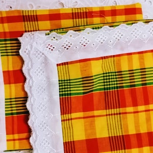 May include: Two pieces of fabric with a checkered pattern in red, yellow, green, and black. The fabric is bordered with white lace.