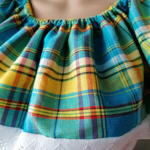 May include: A blue, yellow, and red plaid fabric with a ruffled neckline. The fabric is gathered at the neckline and has a white lace trim.