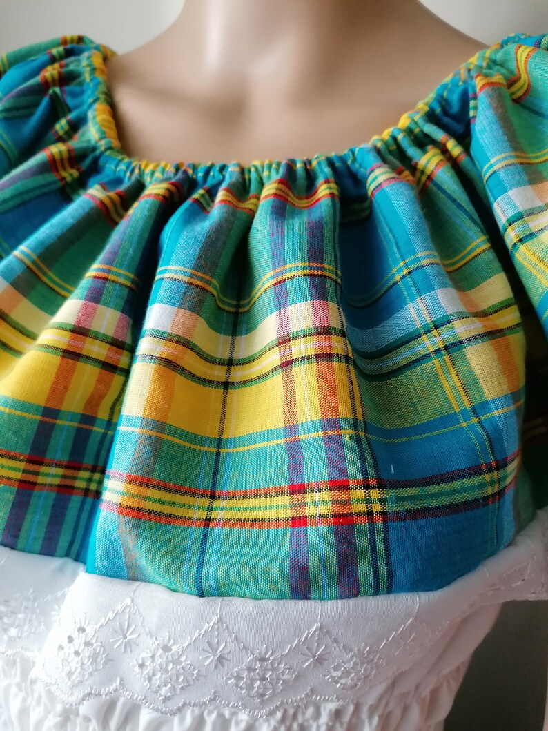 May include: A blue, yellow, and red plaid fabric with a ruffled neckline. The fabric is gathered at the neckline and has a white lace trim.