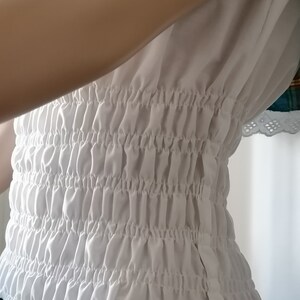 May include: White gathered elastic waistband with a zipper closure. The waistband is made of a soft, lightweight fabric.