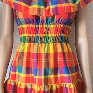 May include: A colourful plaid off-the-shoulder dress with a ruffled neckline and a gathered waist. The dress has a short, A-line silhouette and is made of a lightweight fabric.