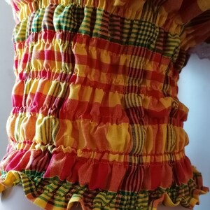 May include: A red, yellow, and green plaid fabric with a gathered, ruffled edge. The fabric is gathered in a series of horizontal rows, creating a textured look.