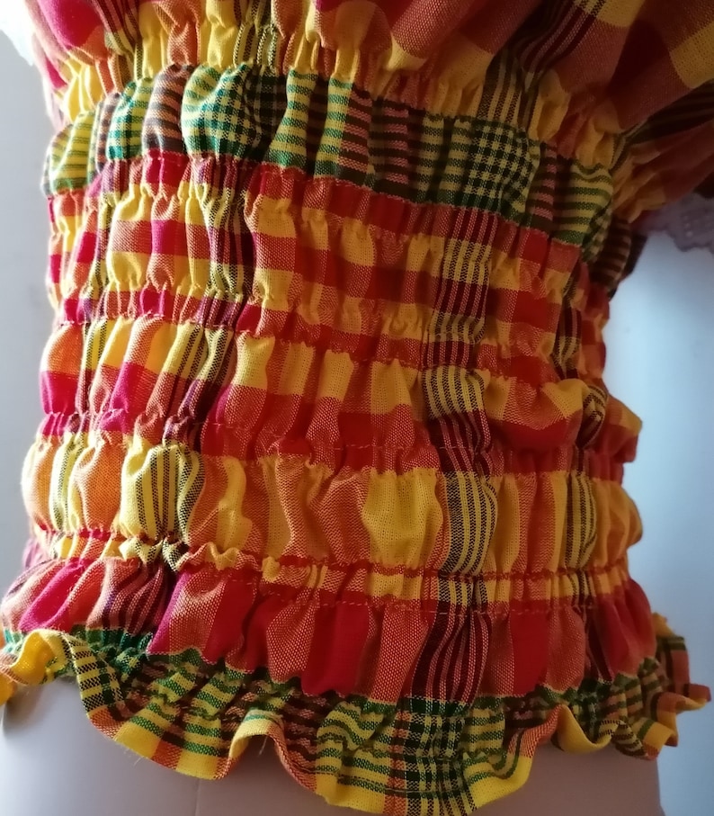 May include: A red, yellow, and green plaid fabric with a gathered, ruffled edge. The fabric is gathered in a series of horizontal rows, creating a textured look.