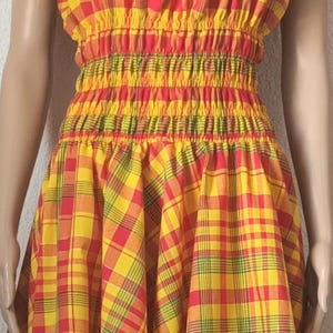 Könnte beinhalten: Ein gelbes, rotes und grünes kariertes Kleid mit einem Rüschenkragen und einem taillierten Oberteil. Das Kleid hat einen gerafften Rock und ist aus einem leichten Stoff gefertigt.