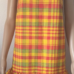May include: A yellow, red, and green plaid dress with a white lace trim around the neckline and hem. The dress has a ruffled hem.