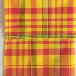 May include: Two red, yellow, and green checkered fabric napkins. The napkins are folded in half and have a woven texture.