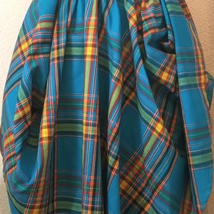 May include: A vibrant, turquoise plaid skirt with an elastic waistband. The plaid pattern features lines of red, yellow, and green. The skirt is gathered, creating a voluminous shape.