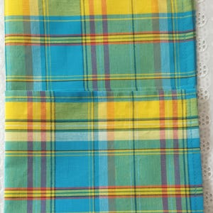 May include: A folded blue, yellow, green, and red plaid fabric with a white background. The fabric has a woven texture.
