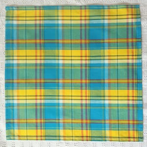 May include: A yellow, blue, green, and red plaid fabric napkin. The napkin is folded and ready to be used.