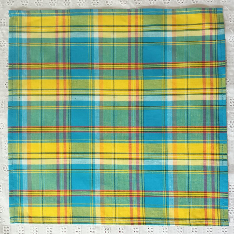 May include: A yellow, blue, green, and red plaid fabric napkin. The napkin is folded and ready to be used.