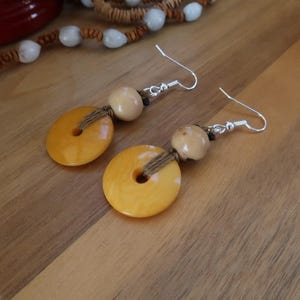 Peut inclure: Une paire de boucles d'oreilles avec des perles en bois jaunes et brunes et des crochets argentés.