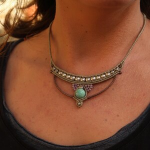 May include: A close-up of a woman wearing a layered necklace with a turquoise stone pendant. The necklace is made of brown cord and silver beads.