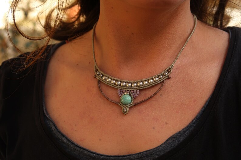 May include: A close-up of a woman wearing a layered necklace with a turquoise stone pendant. The necklace is made of brown cord and silver beads.