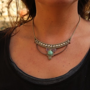 May include: A close-up of a woman wearing a necklace with a turquoise stone pendant and a beaded design. The necklace is made of brown cord and has a silver-colored accent.