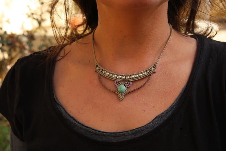 May include: A close-up of a woman wearing a necklace with a turquoise stone pendant and a beaded design. The necklace is made of brown cord and has a silver-colored accent.