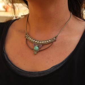 May include: A layered necklace with a turquoise stone pendant and silver beads. The necklace is made of brown cord and has a bohemian style.