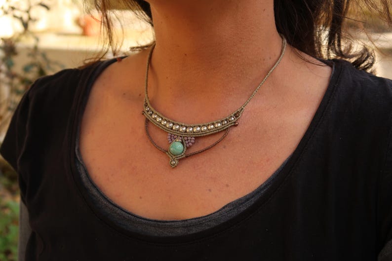 May include: A layered necklace with a turquoise stone pendant and silver beads. The necklace is made of brown cord and has a bohemian style.
