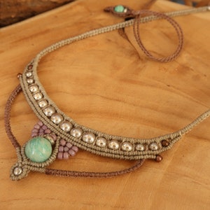 May include: A light green stone pendant necklace with silver beads and brown cord. The necklace is knotted and has a simple design.