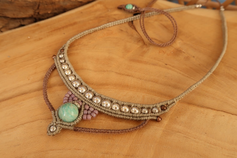 May include: A light green stone pendant necklace with silver beads and brown cord. The necklace is knotted and has a simple design.