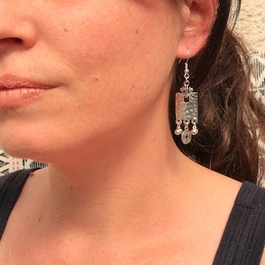 Pode incluir: Brincos de prata com um charme quadrado martelado e pequenas contas redondas. Os brincos têm um fecho de gancho.