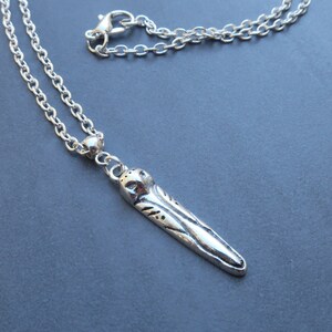 May include: A silver chain necklace with a silver pendant shaped like a long, thin feather with detailed etching.