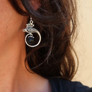 May include: Silver earrings with a black bead and a detailed bird design.