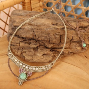 May include: A light green stone pendant necklace with a brown cord and silver beads. The necklace is displayed on a piece of driftwood.