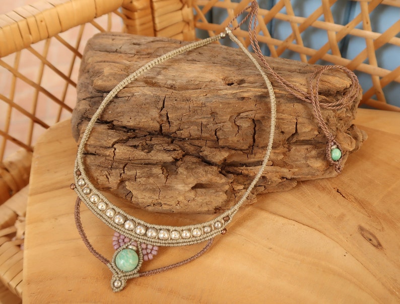 May include: A light green stone pendant necklace with a brown cord and silver beads. The necklace is displayed on a piece of driftwood.