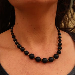 May include: A black beaded necklace with gold accents. The beads are round and have a matte finish.