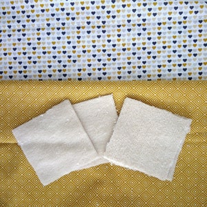 Op de afbeelding: Drie cr&egrave;mekleurige katoenen washandjes op een gele en witte geometrische stoffen achtergrond.