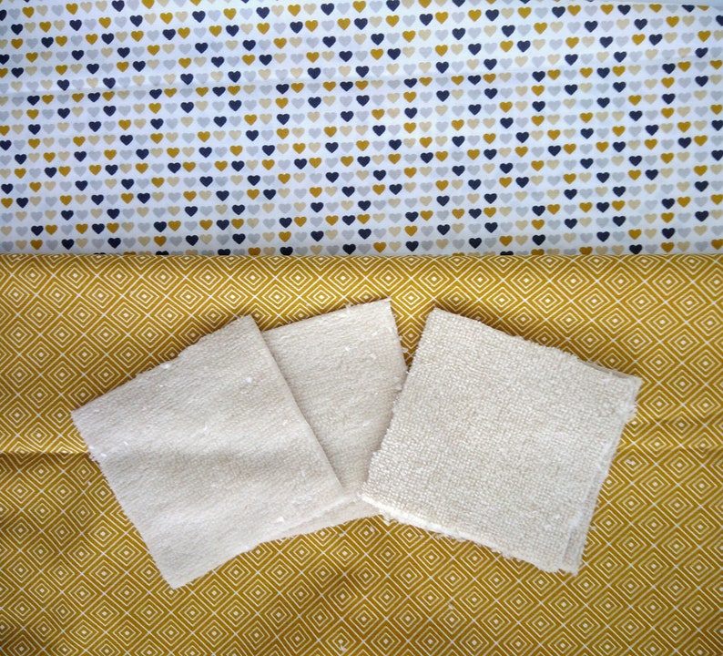 Op de afbeelding: Drie cr&egrave;mekleurige katoenen washandjes op een gele en witte geometrische stoffen achtergrond.