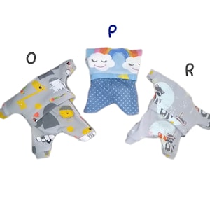 K&ouml;nnte beinhalten: Drei graue und blaue Hundepyjamas mit verschiedenen Mustern. Einer hat einen Regenbogen und Wolken, einer eine Giraffe und eine Katze und einer einen Waschb&auml;ren.