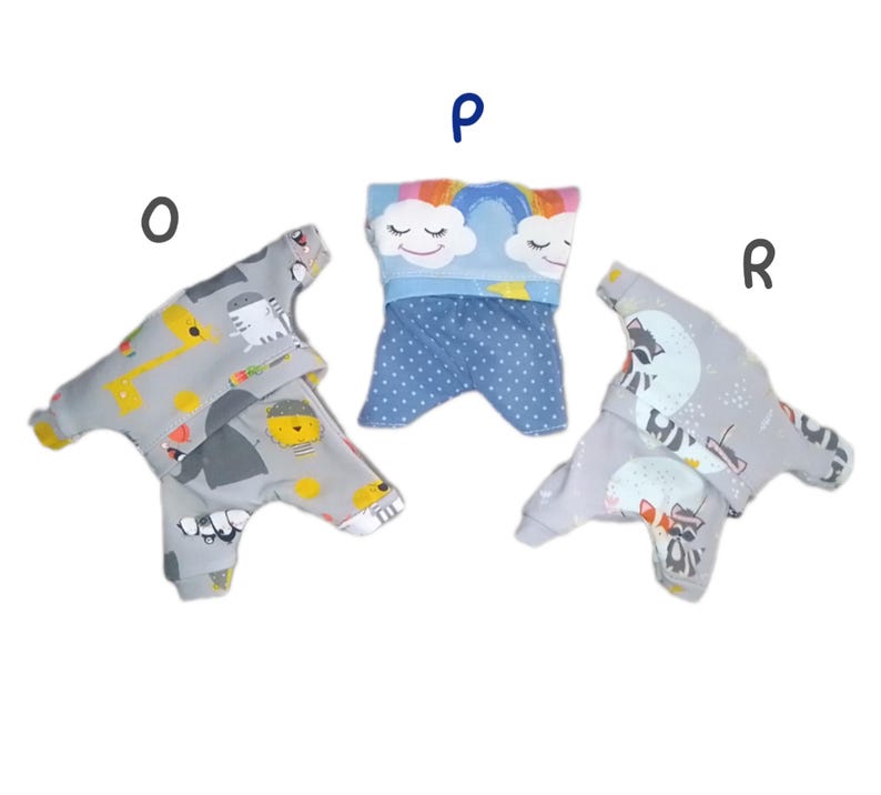 K&ouml;nnte beinhalten: Drei graue und blaue Hundepyjamas mit verschiedenen Mustern. Einer hat einen Regenbogen und Wolken, einer eine Giraffe und eine Katze und einer einen Waschb&auml;ren.