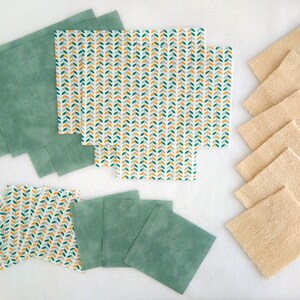 Op de afbeelding: Een set herbruikbare voedselverpakkingen in groen en wit met een bladmotief, en een set beige keukendoeken.