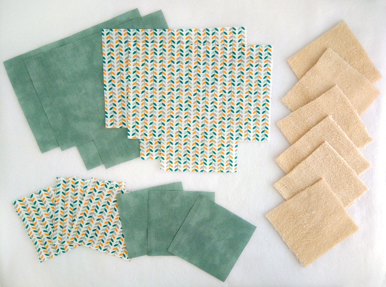 Op de afbeelding: Een set herbruikbare voedselverpakkingen in groen en wit met een bladmotief, en een set beige keukendoeken.