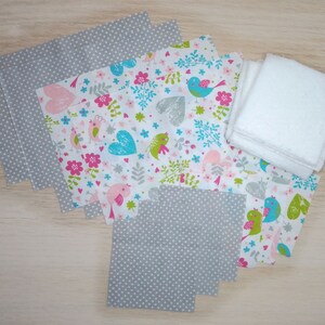 Op de afbeelding: Een set stoffen vierkanten voor knutselprojecten. De vierkanten hebben een grijs stippenpatroon en een witte achtergrond met roze, blauwe en groene vogels en harten. Er zijn ook witte badstof vierkanten.