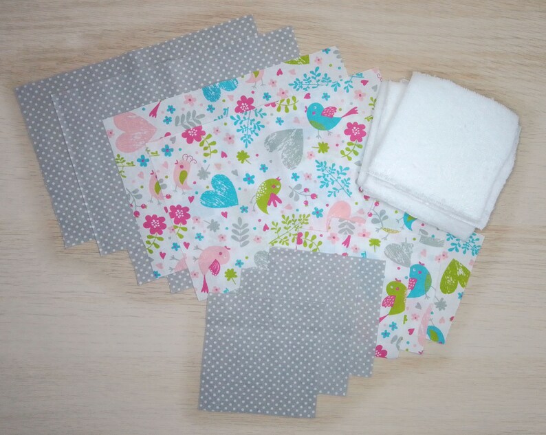 Op de afbeelding: Een set stoffen vierkanten voor knutselprojecten. De vierkanten hebben een grijs stippenpatroon en een witte achtergrond met roze, blauwe en groene vogels en harten. Er zijn ook witte badstof vierkanten.