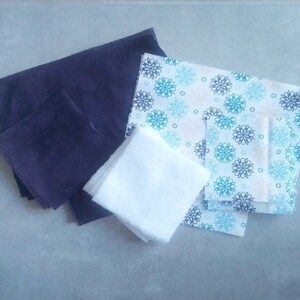 Op de afbeelding: Een set stoffen vierkanten in verschillende kleuren en patronen. De set bevat een donkerblauw vierkant, een wit vierkant en een gepatroneerd vierkant met blauwe en witte bloemen.