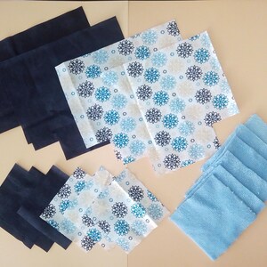 Op de afbeelding: Een verzameling stoffen vierkanten in verschillende kleuren en patronen. Er zijn blauw-witte gepatroneerde vierkanten, effen blauwe vierkanten en effen zwarte vierkanten.