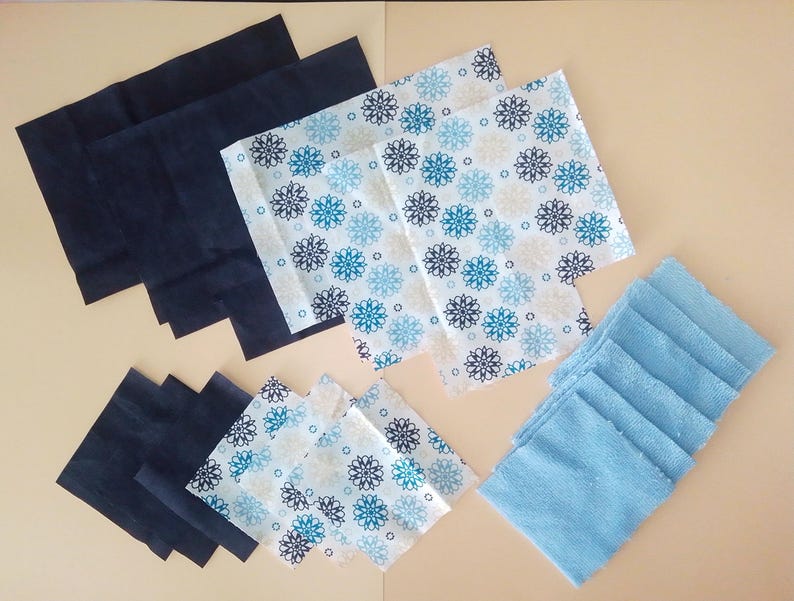 Op de afbeelding: Een verzameling stoffen vierkanten in verschillende kleuren en patronen. Er zijn blauw-witte gepatroneerde vierkanten, effen blauwe vierkanten en effen zwarte vierkanten.