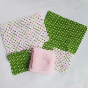 Op de afbeelding: Assortiment van stoffen vierkanten in roze, groen en wit met verschillende patronen, waaronder harten en een geometrisch ontwerp. Een roze washandje is ook inbegrepen.
